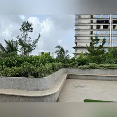 A close-up of the custom-designed, curved concrete planters that serve as integrated seating. The smooth finish of the bench is set against a backdrop of dense, layered shrubs and trees, offering a comfortable spot within the green campus.