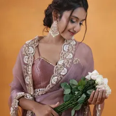A soft and romantic portrait of a model in a lavender organza saree with a scalloped, embroidered border. The sequined blouse and bouquet of white roses add a touch of modern elegance, perfect for occasion wear lookbooks.