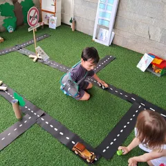 Two children play with wooden cars on the roads of our miniature town. This kind of play helps them understand concepts like traffic, directions, and community layouts.