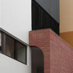 A detail shot of the Franklin Residence, showing the junction of three different materials: red brick, a black metal screen, and smooth white plaster. The clean lines and careful composition create a visually interesting architectural detail.