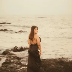 A moody, sepia-toned portrait on a rocky beach. The overcast light and the vastness of the sea create a pensive and atmospheric shot, focusing on emotion and environment.