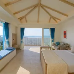 Another view of the bedroom in the Goa holiday home, showcasing the vaulted ceiling with exposed wooden beams and a built-in window seat. This design choice adds rustic charm and creates a cozy nook to enjoy the expansive views.
