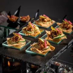 A close-up of our modern take on a classic snack. These crispy nacho-style bites are topped with a savory mixture and pickled onions, served on individual glass plates for an elegant presentation at a Diwali party.