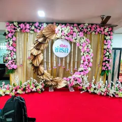 A modern take on a traditional backdrop. This stage for a Sreemantham ceremony uses a circular floral arch of pink and white roses, accented with golden palm leaves against a simple gold curtain, blending contemporary design with classic elements.