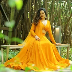 A model seated gracefully in a vibrant yellow-orange lehenga, framed by lush greenery. This shot combines fashion with nature, creating a serene and beautiful campaign image.