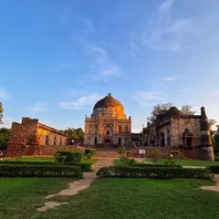 A wide landscape shot of Lodi Garden at sunset. The warm light on the tomb and the beautiful sky create a picturesque and peaceful scene.