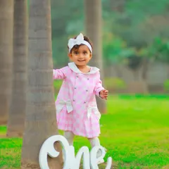 A classic first birthday portrait in the park. This little girl's adorable pink coat and the simple "One" prop make for a sweet and timeless memory of her turning one.