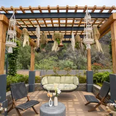 A cozy and stylish seating nook under a wooden pergola. The setup features a modern swing, comfortable chairs, and hanging macrame planters, creating a perfect spot to relax.