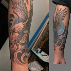 A full eagle sleeve tattoo with a blue sky background. The design wraps around the forearm, showing the eagle in a dynamic pose. It's a symbol of power and freedom that makes a bold statement.