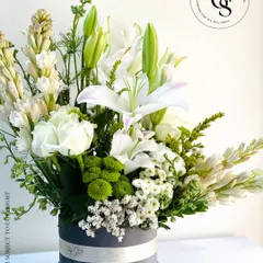 An elegant and serene floral arrangement in a grey velvet hatbox. This stunning bouquet features white lilies, tuberoses, and roses, creating a classic and timeless look of pure sophistication.