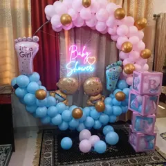 Another popular design for a baby shower or gender reveal. This setup features a circular balloon arch with blue on the bottom and pink on top, a neon sign, and "It's a Boy" and "It's a Girl" foot-shaped foil balloons.