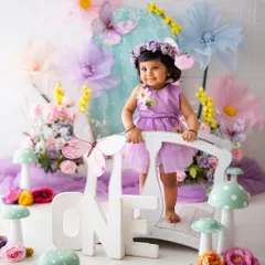 One year old and full of wonder! Standing on a bridge in a pastel fairy garden, this baby girl is celebrating her first birthday in the most enchanting way.