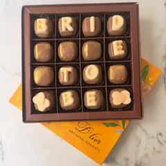 Celebrate the bride-to-be with a personal touch. This box of custom chocolates spells out "BRIDE TO BE" in elegant white chocolate lettering on milk chocolate squares, offering a sweet and memorable gift for bridal showers and pre-wedding celebrations.