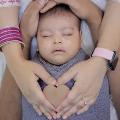 A close up shot showing parents' hands forming a heart around their sleeping newborn. This pose is a beautiful way to symbolize the love and protection surrounding the newest member of the family.