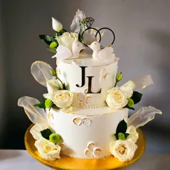 A classic and elegant two-tiered engagement cake in white and gold. It's adorned with fresh white roses, delicate rice paper sails, and two sweet lovebird toppers.