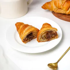 A delicious Nutella-filled croissant, cut in half to show the generous filling, placed on a white plate with a golden spoon. This shot is perfect for a bakery or cafe's dessert menu, highlighting the indulgent treat.