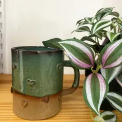 A sweet, heart-stamped mug with a lovely green glaze. This piece is perfect for gifting to a loved one or for adding a touch of warmth to your own mug collection.