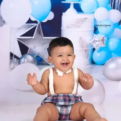 A wide-eyed and happy baby boy, covered in cake and smiling from ear to ear. This shot captures the delightful mess and excitement of a first birthday cake smash.