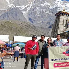 **Group Smiles in Front of Kedarnath Temple.** Our happy clients posing with the Manchala Mushafir banner against the magnificent backdrop of the Kedarnath temple and Himalayan peaks.