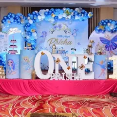 A classic first birthday celebration with a "Little Angel" theme. The decor features large illuminated "ONE" letters, a blue and white color scheme, and butterfly accents on the backdrop and pedestals.
