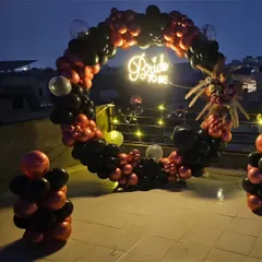 A bold and stylish rooftop bachelorette party setup. The circular balloon arch in black and metallic red frames a "Bride to be" neon sign, creating a dramatic photo backdrop against the night sky.