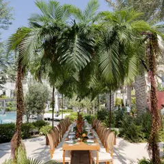 A long dining table set for a welcome lunch under a canopy of palm fronds. This tropical-themed tablescape creates a unique and immersive dining experience.