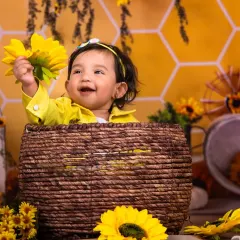 A bright and cheerful baby girl enjoying the sunflower props in our bee-themed shoot.