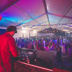 The view from my DJ booth at a packed dandiya night under a large tent. The colorful flags and enthusiastic crowd create an amazing atmosphere for a wedding sangeet.