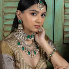 This bridal set features layered Kundan necklaces with emerald drops and delicate pearls, paired with matching jhumka earrings and a maang tikka. It's a complete look that exudes grace and sophistication for the modern bride.