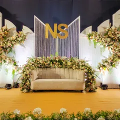 A wider view of the modern "NS" Sangeet stage, showing the asymmetrical floral arrangements and the elegant contrast between the dark backdrop and white panels.
