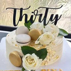 Thirty has to be special! An elegant white and gold cake for a 30th birthday, decorated with fresh white roses, macarons, and gold leaf.