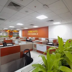 We used biophilic design principles in this workstation area, incorporating lush green planters to separate spaces and improve ambiance. The "Work Hard Stay Humble" wall graphic reinforces company values within the daily workspace.