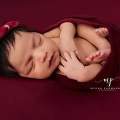 A close-up of a sleeping newborn in a deep red wrap, highlighting their perfect features and peaceful expression. This is a classic newborn portrait.