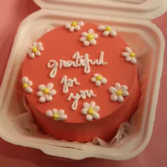 A lovely coral-colored bento cake with the message "grateful for you" and decorated with small daisies. A sweet way to show appreciation.