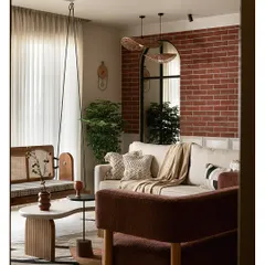 As you enter this living area, an exposed brick wall creates a warm, earthy backdrop. I placed a large arched mirror to reflect natural light, making the space feel larger and connected to the outdoors. The custom reversible cane swing, organic-shaped tables, and rich textures come together to create a grounded yet elegant feel.