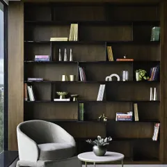 A reading nook with a view. The dark, full-height bookshelf creates a dramatic, library-like feel, while the comfortable armchair is perfectly positioned to take advantage of the natural light from the large window.