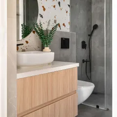 This bathroom combines modern and rustic styles with a playful terrazzo tile accent wall. The wood vanity adds warmth, and the sleek black fixtures provide a contemporary touch.