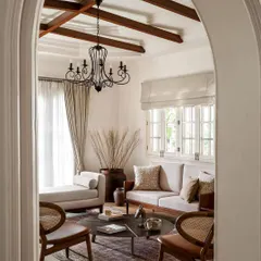 This view into the living room, captured by Architectural Digest, showcases the home's character. The design features exposed wooden ceiling beams, a classic chandelier, and a mix of modern and cane furniture, reflecting my philosophy of layering textures and eras.