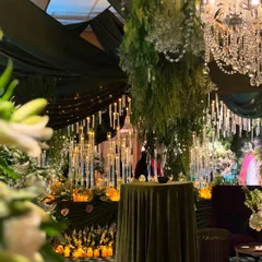 A view into the 'Enchanted Woods' theme, with a focus on the thousands of hanging and standing candles. The warm glow contrasts beautifully with the deep green drapery and lush foliage.