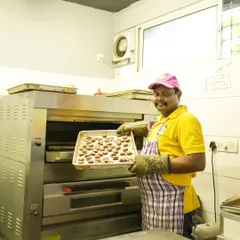Baking happiness is a team effort. A smiling chef holds a tray of freshly baked treats, showcasing the love and care we put into our work.