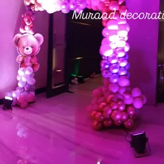 An entrance arch for a teddy bear themed party. The arch is made of pink and metallic balloons, with a teddy bear foil balloon integrated into the design to welcome guests.