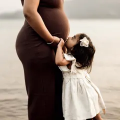 An incredibly tender moment between a mother and daughter by the water. The little girl gives her mom's baby bump a sweet kiss, a beautiful display of sibling love before they've even met.