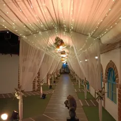 A beautiful, long walkway decorated with a canopy of draped fabric and fairy lights. The path is lined with floral arrangements, creating an elegant and dreamy entrance for a resort wedding.