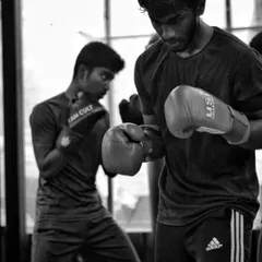 Two fighters training side by side, one on the bag and one shadow boxing. The energy in the gym is about shared, focused work.
