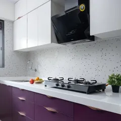 This kitchen from 'The Adobe' project features a bold pop of color with deep purple lower cabinets. The design is balanced with white upper cabinets, a white countertop, and a modern terrazzo-style backsplash.