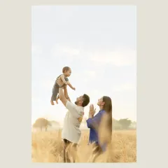 A moment of pure joy as a father lifts his child high into the air, with mom looking on with love. Set against the backdrop of a golden field, this image captures the energy and happiness of a young family enjoying a beautiful day together.