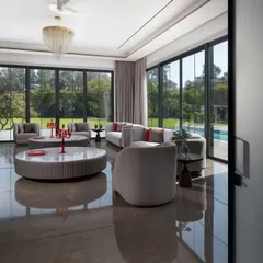 The reflection on the polished marble floor doubles the light and greenery in this expansive living area. Our material choices are intentional, designed to enhance the sense of space and luxury.