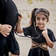 A creative maternity shot where the older sister playfully uses a stethoscope on her mother's baby bump. A sweet way to include siblings in the journey.