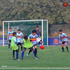 A young player in a green bib shields the ball from two opponents during a competitive match. This shows the toughness and game intelligence we develop.