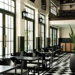 A view of the main dining hall at Elgin Cafe, showcasing the rhythmic repetition of tall, black-framed windows that flood the space with natural light. The design balances the graphic floor with the calm of the white walls.